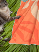 Cat interacting with an orange towel with leaf pattern on green grass