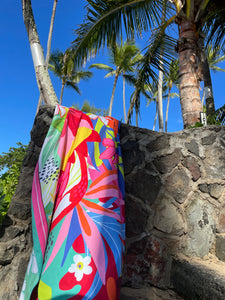 Close up of Suzanne Jennerich x Surfer Towel signature print.  Towel draped over a rock wall on the beach with palm trees in the background.